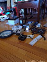 Photo showing multiple clocks and watches arranged on a wooden floor including decorative plastic cuckoo clocks, desk clocks, and watches in boxes.