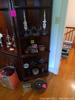 Candlesticks on shelf with crystal candy dishes, wooden bowls, small silver tray, brass bowl and other small items on lower shelf and floor.