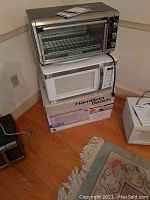 Photo showing Black & Decker toaster convection oven placed on top of a white Hamilton Beach microwave oven and its box beside it.