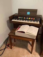 Full view of the vintage Lowery organ with bench and open music book showing sheet music on top of the bench.