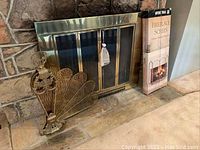 Brass fan-style fireplace screen placed in front of a stone fireplace with metal glass doors.