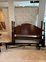 Two solid wood headboards with turned posts and one black metal bed frame laid on carpeted floor near white mattresses in basement.