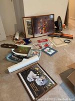 Wide view showing multiple framed art prints and posters displayed on floor, including floral painting, dog print, Coca-Cola poster, and various smaller items scattered around.