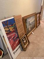 Collection of framed art and posters stacked against a wall showing various sizes and frames