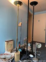 Three floor lamps and several table lamps and light fixtures arranged on blue carpet against a beige wall.