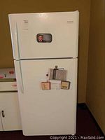 Front view of the closed white Frigidaire refrigerator with top freezer and papers attached to the door.