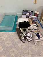 Full lot overview showing mixed beauty and personal care items including a clear plastic bin lid, hairdryers, curling irons, and boxed items.