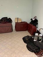 Soft side luggage and bags arranged on floor against white wall, showing various pieces in burgundy, brown, black, and patterned tote bags.