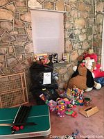 Wide view showing various toys including plush penguin, plastic Easter eggs, bins of small toys, black bags and a stone wall background.