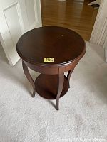 Side view of small round wood side table showing four curved legs and lower circular shelf, dark brown finish, light surface wear on top