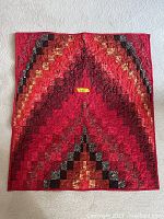 Full view of small handmade quilt with red, black, brown, and cream fabric squares forming a geometric pattern.