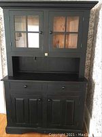 Front view of black painted solid wood kitchen hutch showing two glass pane upper doors, open shelf, two drawers and two lower cabinet doors