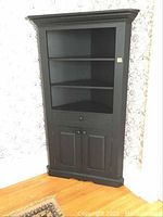 Full front view of the black painted solid wood corner hutch showing open shelves, false front drawer, and closed bottom cabinet doors.