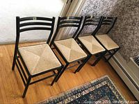 Four black painted ladder-back chairs with natural cane seats arranged in a row on hardwood floor