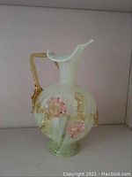 Front view showing delicate swirled uranium glass with applied gold-tone floral decorations and curved handle.