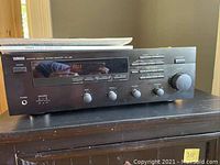 Front view of Yamaha RX-495/395 stereo receiver powered on showing 'AUX' on the digital display. Unit has knobs and buttons on front panel with a black finish.