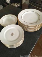 Set of stacked white plates with gold rims, showing dinner and side plates in two stacks on a dark surface.