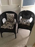Pair of two black rattan tub style chairs with floral patterned cushions placed next to each other on carpet.
