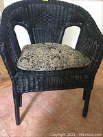 Front view of black rattan tub style chair with ornate patterned cushion, showing woven rattan construction and overall shape.