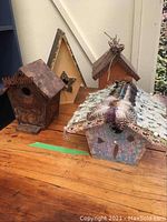 Four whimsical handcrafted bird houses of different styles and sizes on wooden floor