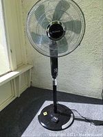 Full view of the Noma oscillating stand fan showing black and chrome design, fan with protective chrome grill and base with remote placed on it
