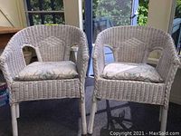 Front view of two white wicker chairs with cushions, showing details of chair shape and cushion pattern.