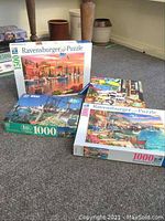 Photo showing four puzzle boxes arranged on carpet; includes three Ravensburger puzzles and one Heye puzzle all unopened.