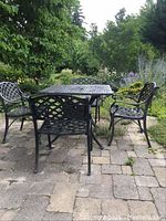 Full view of square table and four chairs on stone patio surrounded by garden
