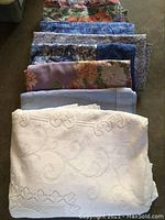 Folded assorted cloth tablecloths with floral patterns and cream embroidered cloth on top