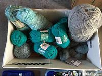 Box of assorted yarn skeins in grey, teal, and variegated colors and textures