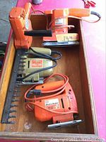 Four Black & Decker tools in wooden drawer: hedge trimmer, hand sander, two-speed jigsaw, and FS1000 sander.