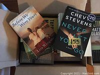 A close-up view inside one box showing books including Before We Were Yours by Lisa Wingate and Never Let You Go by Chevy Stevens with a price sticker.