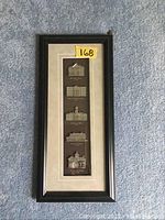 Full view of framed cast metal relief replicas of historic Cobourg buildings with five labeled pieces mounted vertically in a black frame with beige matting.