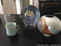 Full set of 4 ceramic artworks on table showing plate, rounded pot, and two mugs.