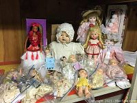 Wide view featuring multiple dolls including Hawaiian-themed doll, baby doll in white bonnet, and clown doll in pink satin costume.