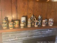 Wide view showing 11 assorted German beer steins arranged on a wooden shelf.