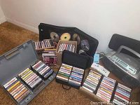Wide shot showing large assortment of cassette tapes in plastic boxes and cases, CD cases and loose CDs arranged around the player