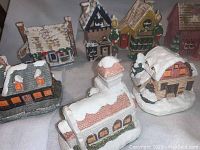 Front view of 6 ceramic village buildings with snow on roofs, varying architectural styles and colors.