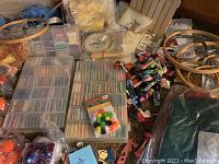 Wide view showing embroidery floss storage cases, loose floss skeins, orange yarn balls, and pom-poms scattered on carpeted floor