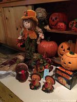 Full group of harvest and Halloween-themed kitchen decor items arranged on shelves and floor in a rustic setting. Includes scarecrow doll, ceramic pumpkins, turkeys, and cornucopia.