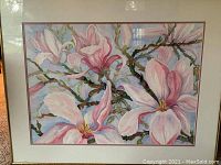 Full view of framed watercolor painting showing pink magnolia flowers and branches against a blue sky background.