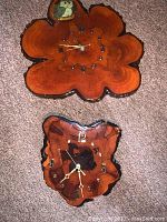 Photo showing both slab clocks lying on carpet; larger clock has painted owl near top, smaller clock with metallic numbers and dots.