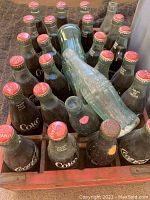 Top view of 26 vintage Coca Cola bottles, 24 filled, some empty or missing caps, in original wooden crate.