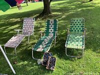 Three vintage aluminum lounge chairs with woven seats and backs shown on green lawn with a box of extra woven strips in front.