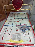 Full view of the vintage tabletop hockey game showing the plastic ice rink, mechanical player rods, goals, and a red goal light indicator structure.