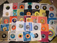 Top view showing assortment of 35+ vintage 45 RPM vinyl records mostly in paper sleeves with varying label designs