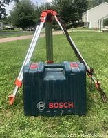Aluminum tripod standing over closed Bosch carrying case on grass