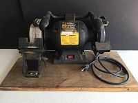 Front view of the bench grinder unit mounted on wooden base with two grinding wheels and power cord.