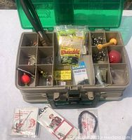 Open double-sided tackle box showing various fishing lures, hooks, sinkers, and small packaged tackle items