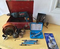Entire lot displayed including vintage red metal case, Bosch hammer drill, various sizes of hole saws, several drill bits, Tapcon installation tools, blue plastic accessory case, and wet diamond hole saw in packaging.